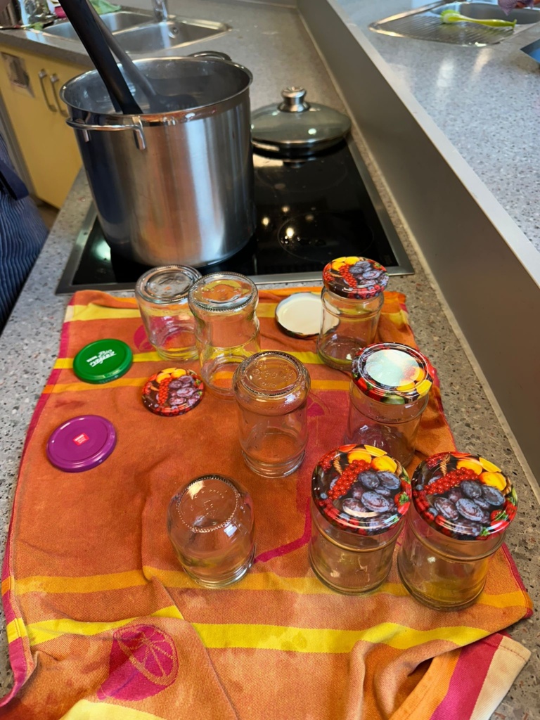 Erdbeer1 Ausgewaschene Schraubgläser stehen auf einem Geschirrhandtuch, dahinter ein dieser Topf mit heißer Marmelade.