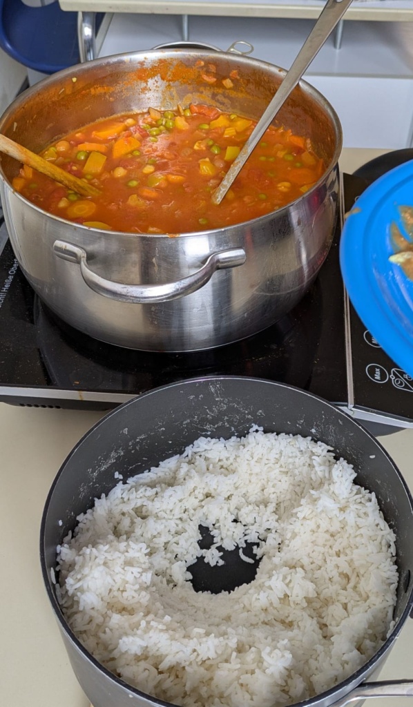 Kulinarik5 Blick von oben in einigen Topf mit weißem Reis und eine tomatiere Suppe mit Erbsen und Möhren.