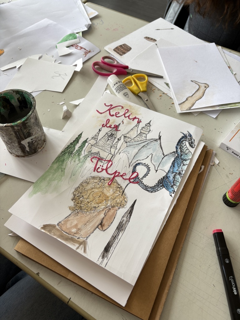 Märchen2 Blick auf den Tisch eines Illustrators, der gerade ein Aquarell zu "Selim,, der Tölpel" zeichnet. Zu sehen sind eine Rückansicht, ein Drache und ein Schloss.