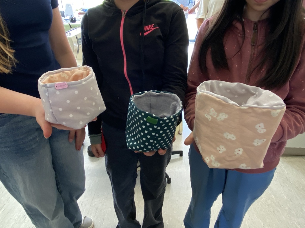 Nähen3 Drei Schülerinnen präsentieren drei genähte Stoffbeutel in verschiedenfarbigen Stoffen.