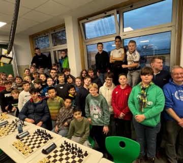 Alle Schachturnierteilnehmenden und die beteiligten Lehrkräfte sind in einem Schulraum mit Schachbrettern zu sehen.