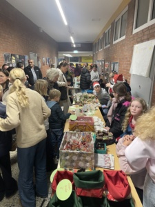 IMG_7385 Gutgelaunte Schülerinnen und Schüler verkaufen weihnachtliche Produkte. Der Gang ist voller Besucher.