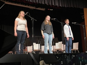 IMG_7400 Ein Trio zweier älterer Schülerinnen und eines Schülers singt auf der Bühne.