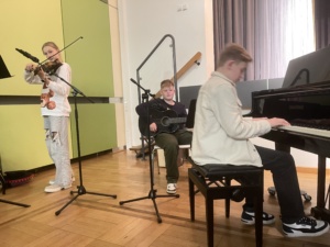 IMG_7408 Drei Lernende spielen Geige, Gitarre und Flügel.